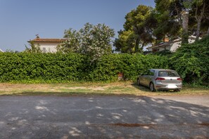 Une voiture est garée sur une allée gravillonnée, avec une haie et un bâtiment en arrière-plan.