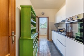 Eine Küche mit einem grünen Schrank, einer Wanduhr und Blick ins Freie.