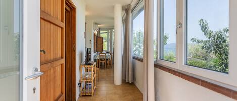 A corridor with wooden doors, a dining area with a table and chairs, and large windows offering a view of greenery and a body of water.
