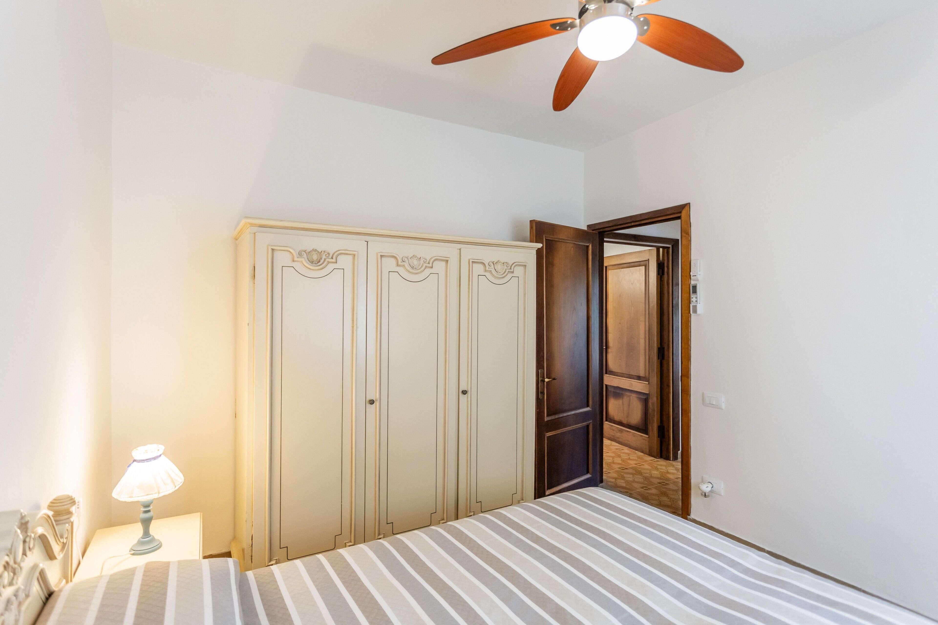 Un dormitorio con cama, armario, ventilador de techo y mesita de noche con lámpara.