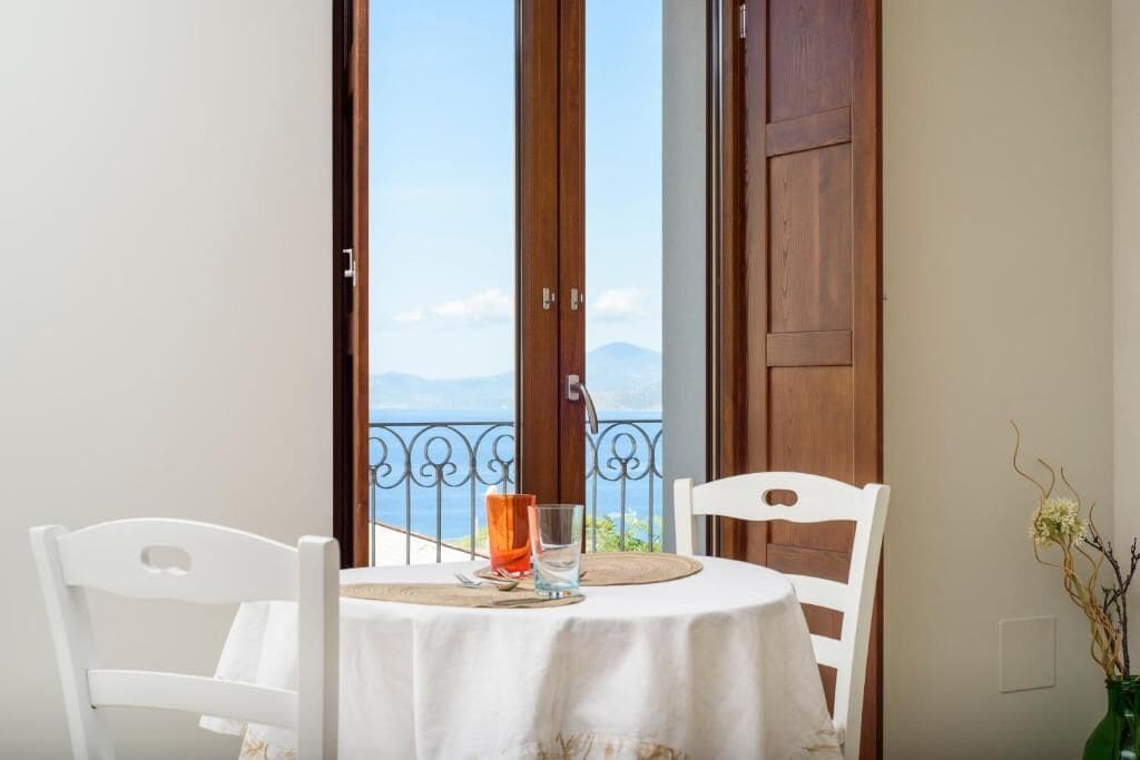 A balcony with a table and chairs, a view of the sea, and a wooden door.