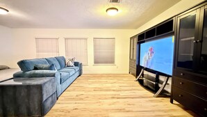 Ein Wohnzimmer mit einem blauen Sofa, einem Fernseher auf einem Schrank und Holzboden.