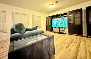 Ein Wohnzimmer mit grauem Sofa, Flachbildfernseher, Holzboden und integrierten dunklen Holzschränken.