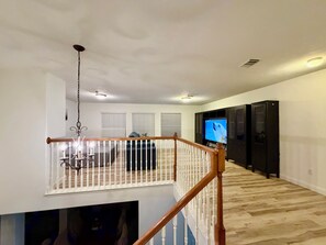 A spacious living area with a high ceiling, a chandelier, a television, and a staircase leading to an upper level. - This is a spacious house with 5 bedrooms and 2.5 bathrooms. many amenities (Houston)