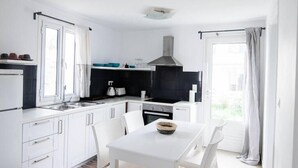 Uma cozinha moderna com armários brancos, painel de fundo preto e um espaço de jantar com mesa e cadeiras brancas.