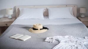 Uma cama bem arrumada com lençóis brancos, um cobertor cinza e um chapéu de palha sobre a cama.