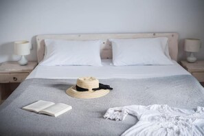 Ein ordentlich gemachtes Bett mit weißer Bettwäsche, einer grauen Decke und einem Strohhut darauf.