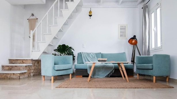 Uma sala de estar com escada, sofá, mesa de centro, abajur e planta.