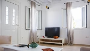 Sala de estar com televisão, sofá, mesa de centro e janela com cortinas.