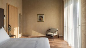A bedroom with a bed, a chair, a painting on the wall, and a window with curtains.
