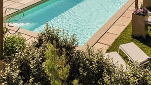 A rectangular swimming pool with clear blue water, surrounded by a paved deck and a glass balustrade.