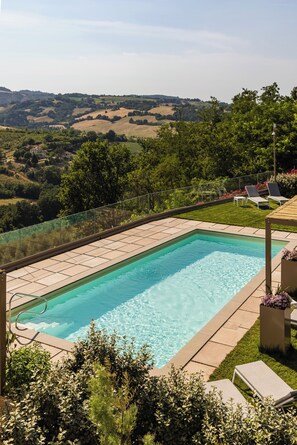 A rectangular swimming pool with clear blue water, surrounded by a paved deck and a glass balustrade.