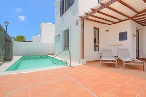 Ein Swimmingpool mit einer Metallleiter, zwei weißen Liegestühlen und einer Pergola.