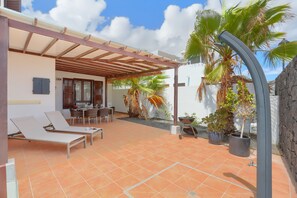 Une terrasse couverte comprenant un espace repas, des chaises longues et des plantes en pot.
