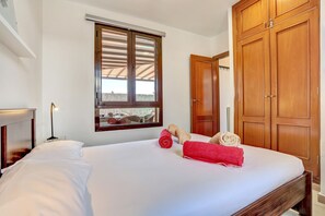 A hotel room with a bed, a window with blinds, wooden wardrobe, and a nightstand with a lamp. - Villa VERO -  Private villa in Playa Blanca (Playa Blanca)