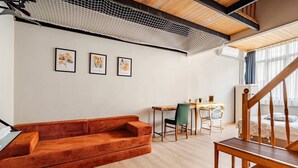 En moderne stue med en træbænk, en rød sofa, et spisebord med stole og en trappe.
