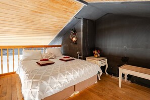 Ein Schlafzimmer mit Holzboden, einem Bett mit weißer Bettwäsche, einem Nachttisch mit einer Vase und einem kleinen Tisch.