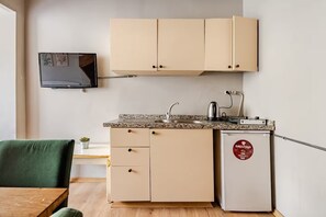 Eine kompakte Küchenzeile mit einem über der Arbeitsplatte montierten Fernseher, einem kleinen Kühlschrank mit Logo und einem Essbereich mit einem grünen Stuhl.