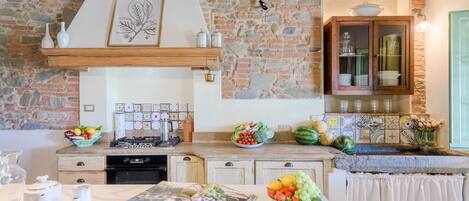 Una cocina con pared de piedra, vigas de madera, estufa a gas, un lavabo y un armario con puertas de vidrio.
