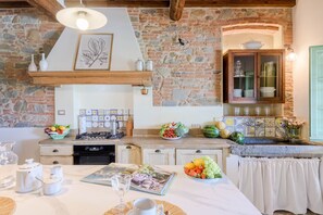 A kitchen with a stone wall, wooden beams, a gas stove, a sink, and a cabinet with glass doors. - Villa Pellegrini with breathtaking view (Montecarlo)