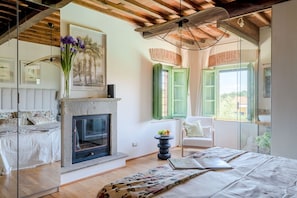 A bedroom with a fireplace, a bed, a chair, and a window with green shutters. - Villa Pellegrini with breathtaking view (Montecarlo)
