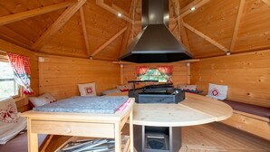 A wooden cabin interior with a central table, seating area, and a fireplace.