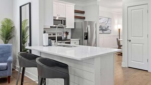 A modern kitchen with white cabinetry, stainless steel appliances, and a marble island with bar stools.