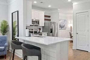 Una cocina moderna con armarios blancos, electrodomésticos de acero inoxidable e isla de mármol con taburetes de bar.