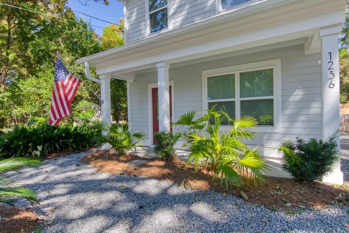 Ein zweistöckiges Haus mit Veranda, Hausnummer 1236, umgeben von tropischen Pflanzen und einer US-amerikanischen Flagge.