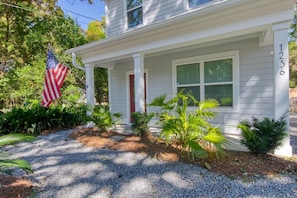 A two-story house with a porch, number 1236, surrounded by tropical plants and an American flag. - Lowcountry Lux, 5 min to Beach, 7 min to Dtwn (Mount Pleasant)