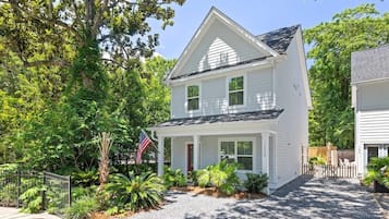 A two-story white house with a front porch, surrounded by lush greenery and an American flag.