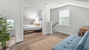 A modern bedroom with a loft-style bed, a blue sofa, and a large window with blinds.