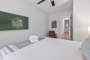 A hotel room with a bed, a chair, a folded towel stack, a painting, and a door leading to another room. - Lowcountry Lux, 5 min to Beach, 7 min to Dtwn (Mount Pleasant)
