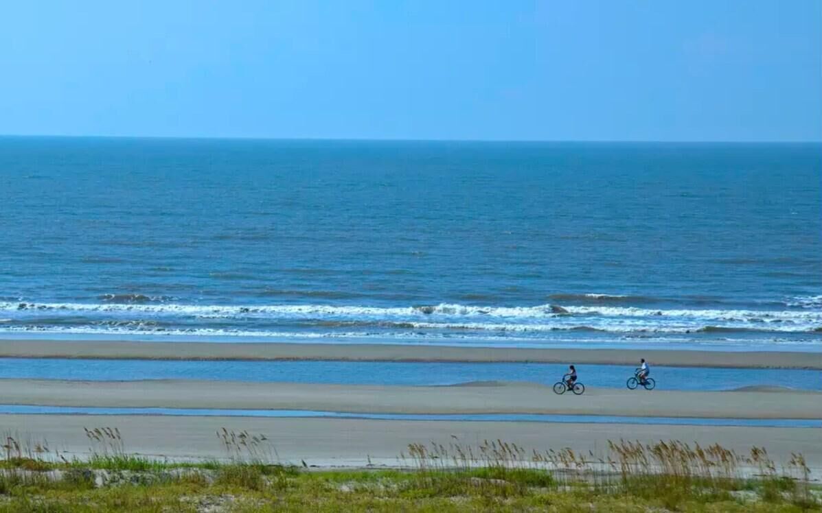 A beach with two cyclists on the sand near the water.
