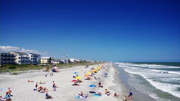 A beach with people sunbathing and swimming, umbrellas, and buildings in the background.