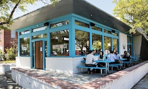 An outdoor seating area with blue tables and chairs, a brick wall, and a sign for a restaurant. - Lowcountry Lux, 5 min to Beach, 7 min to Dtwn (Mount Pleasant)