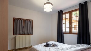 Hotellihuone, jossa on sänky, patteri, ikkuna verhoilla ja kattovalaisin.