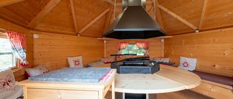 A wooden cabin interior with a dining table, bench seating, and a fireplace.