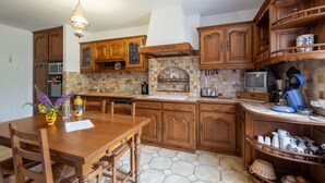 A kitchen with wooden cabinets, a dining table, chairs, a coffee maker, and a television.