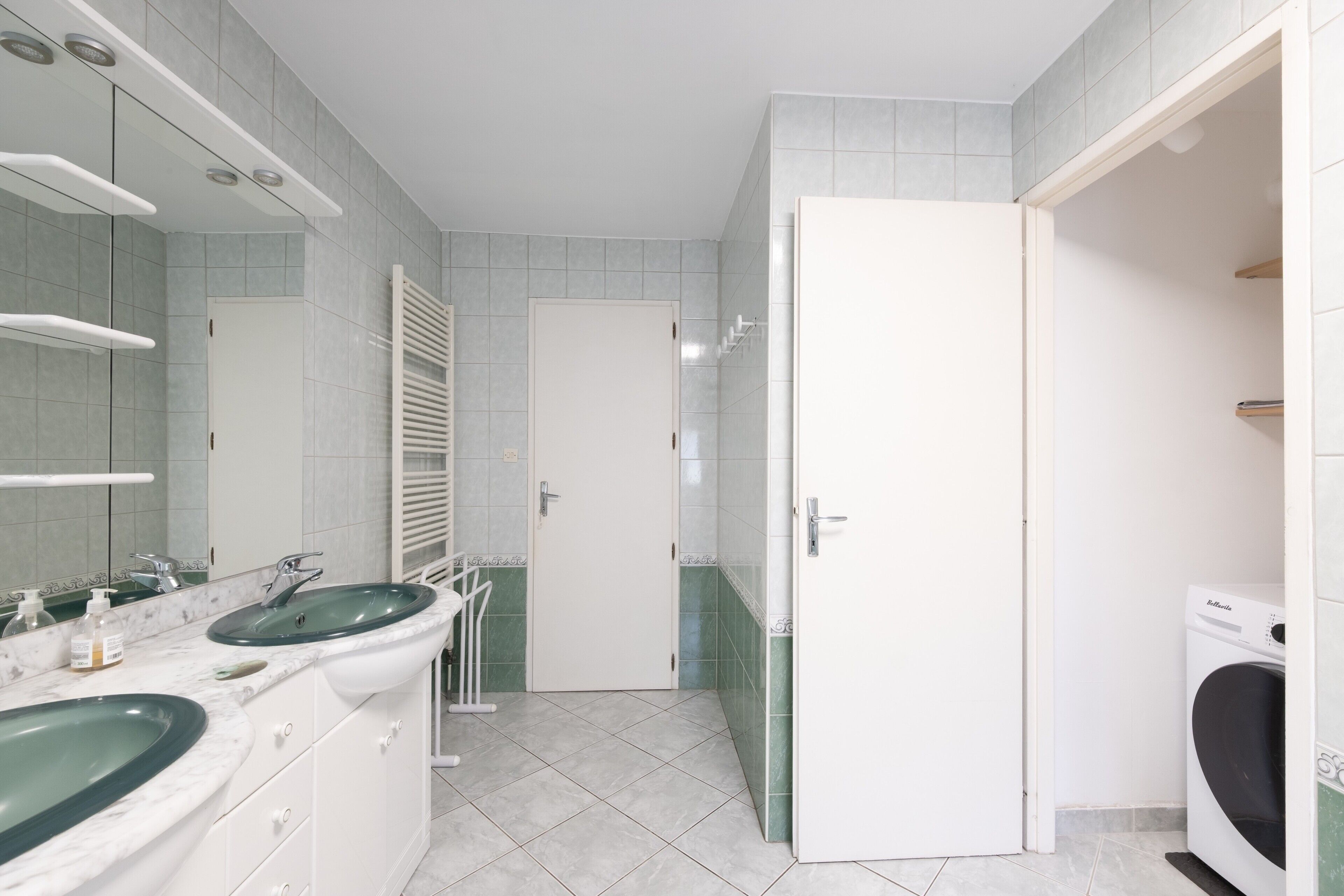 Ein modernes Badezimmer mit einer in Glas eingefassten Dusche, einem weißen Waschbecken mit Marmorplatte und einer weißen Tür zu einem weiteren Raum.