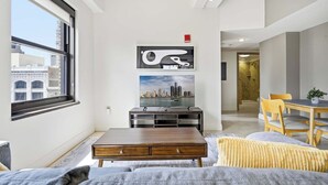 A modern living room with a city view, a dining area with yellow chairs, and a staircase leading to another level. - 2 BR Iconic Detroit High-Rise Loft (Detroit)