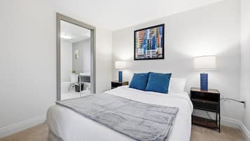 A hotel room with a bed, a nightstand, a lamp, a mirror, and a cityscape painting.