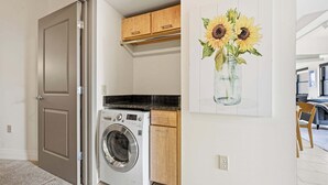 A laundry room with a front-loading washer and dryer, wooden cabinets, and a painting of sunflowers on the wall. - 2 BR Iconic Detroit High-Rise Loft (Detroit)