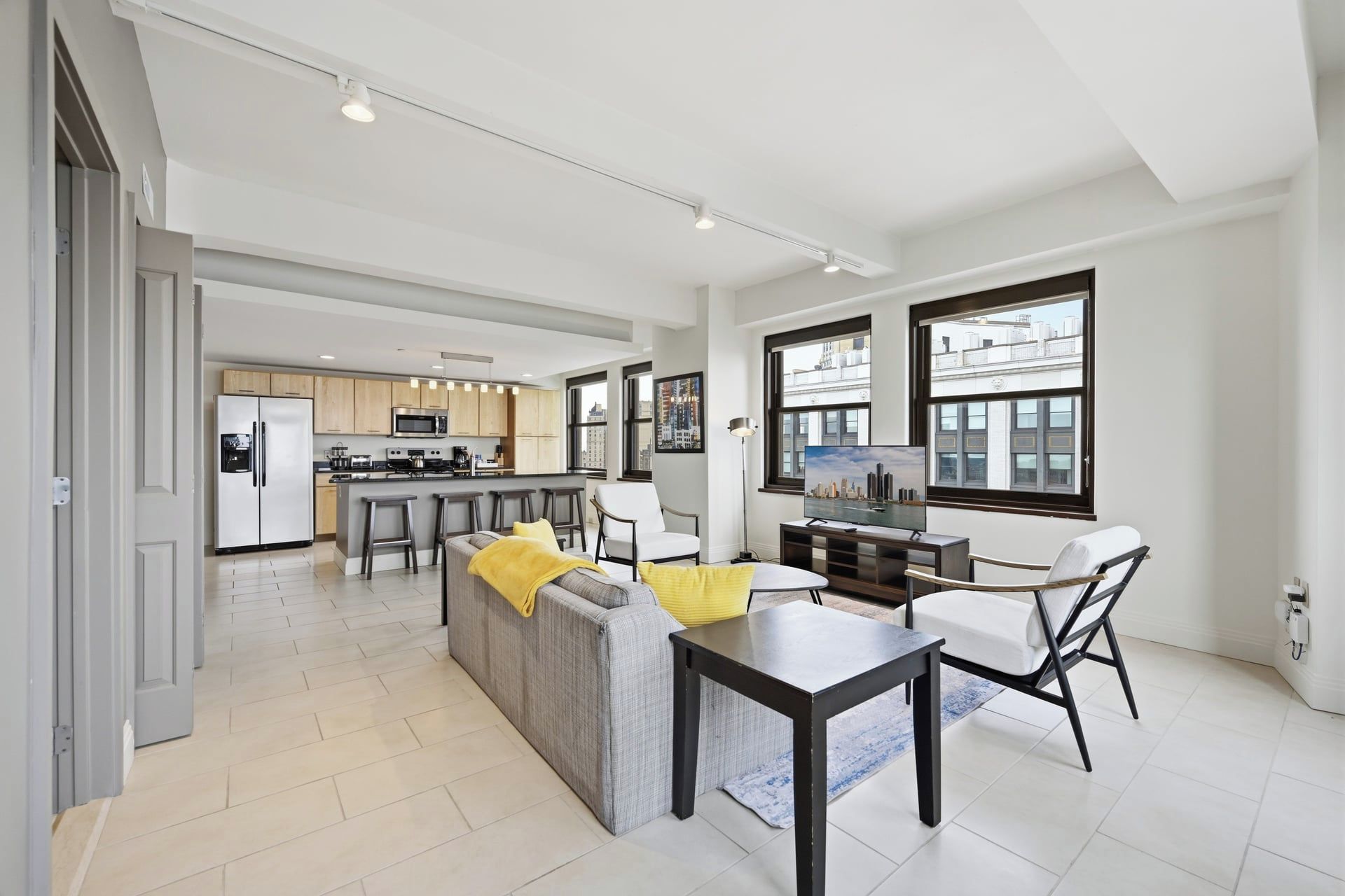 A modern kitchen with a central island, a dining area with a table and chairs, and a living area with a sofa and a TV.