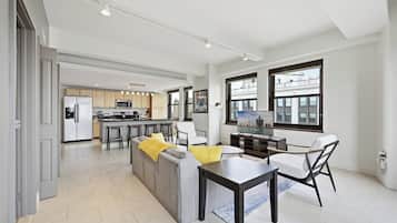 Een moderne keuken met een centraal eiland, een eethoek met een tafel en stoelen, en een zithoek met een bank en een televisie.
