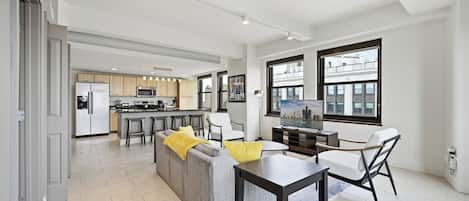 A modern kitchen with a central island, a dining area with a table and chairs, and a living area with a sofa and a TV.