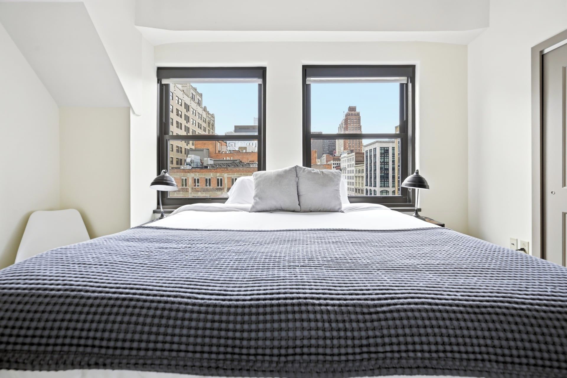 A hotel room with a large bed, two windows, and a view of the cityscape.