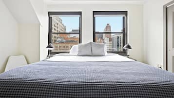 A hotel room with a large bed, two windows, and a view of the cityscape.