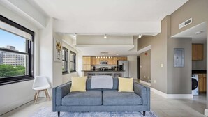 A modern living room with a grey sofa, a coffee table, and a view of the kitchen.