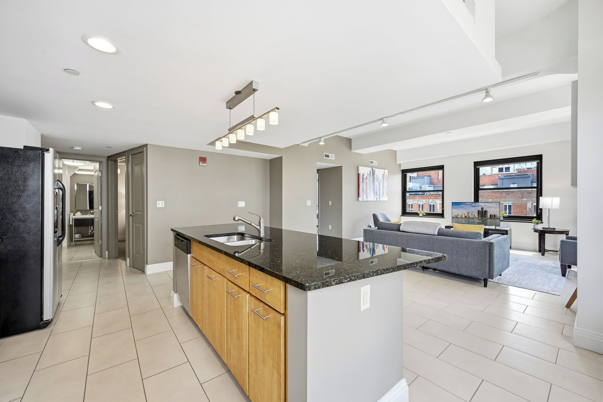 A modern kitchen with a central island, a dining area with a sofa, and a view of buildings through large windows.